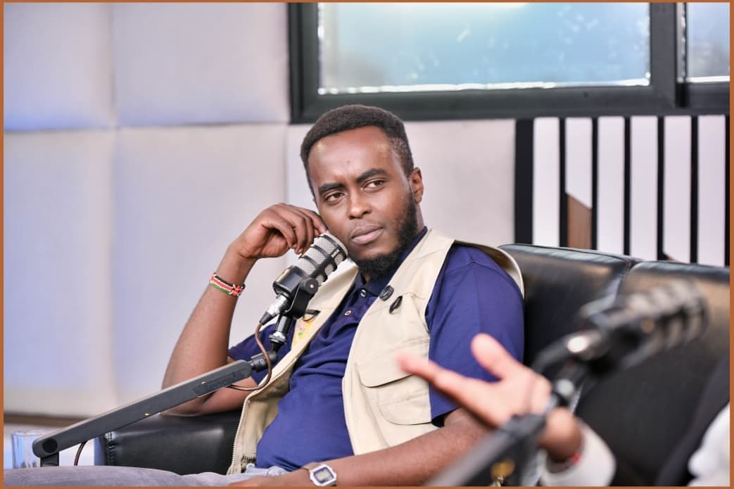 Denzel Maina looking across at a guest, whose hand is just in frame, during a recording