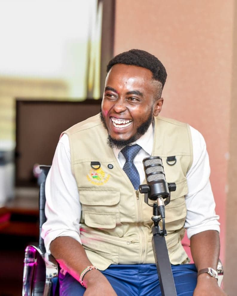 Denzel Maina laughing at a studio microphone, with a Kenyan flag beside him